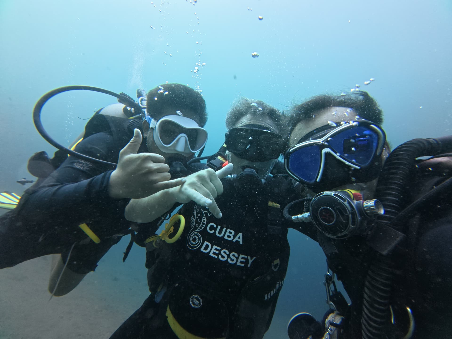 Tres buceadores juntos en agua azul, haciendo señales tranquilas a la cámara.