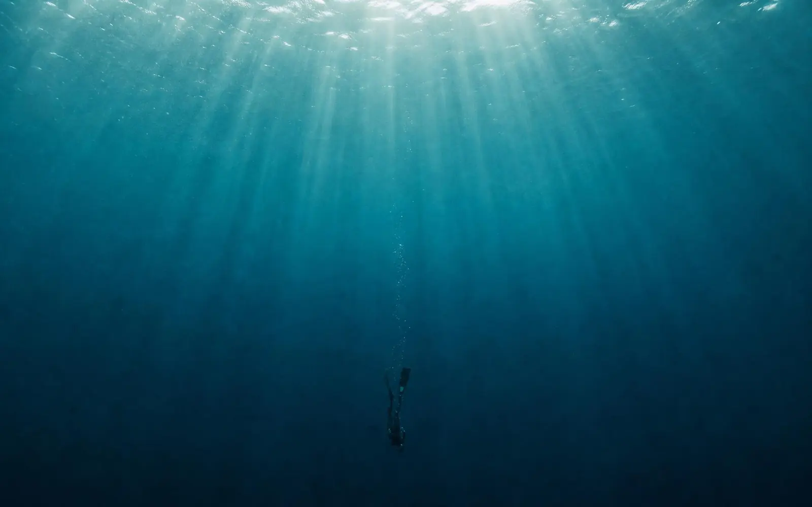 Una apneísta desciende en solitario a través de rayos de luz en aguas azul turquesa profundas